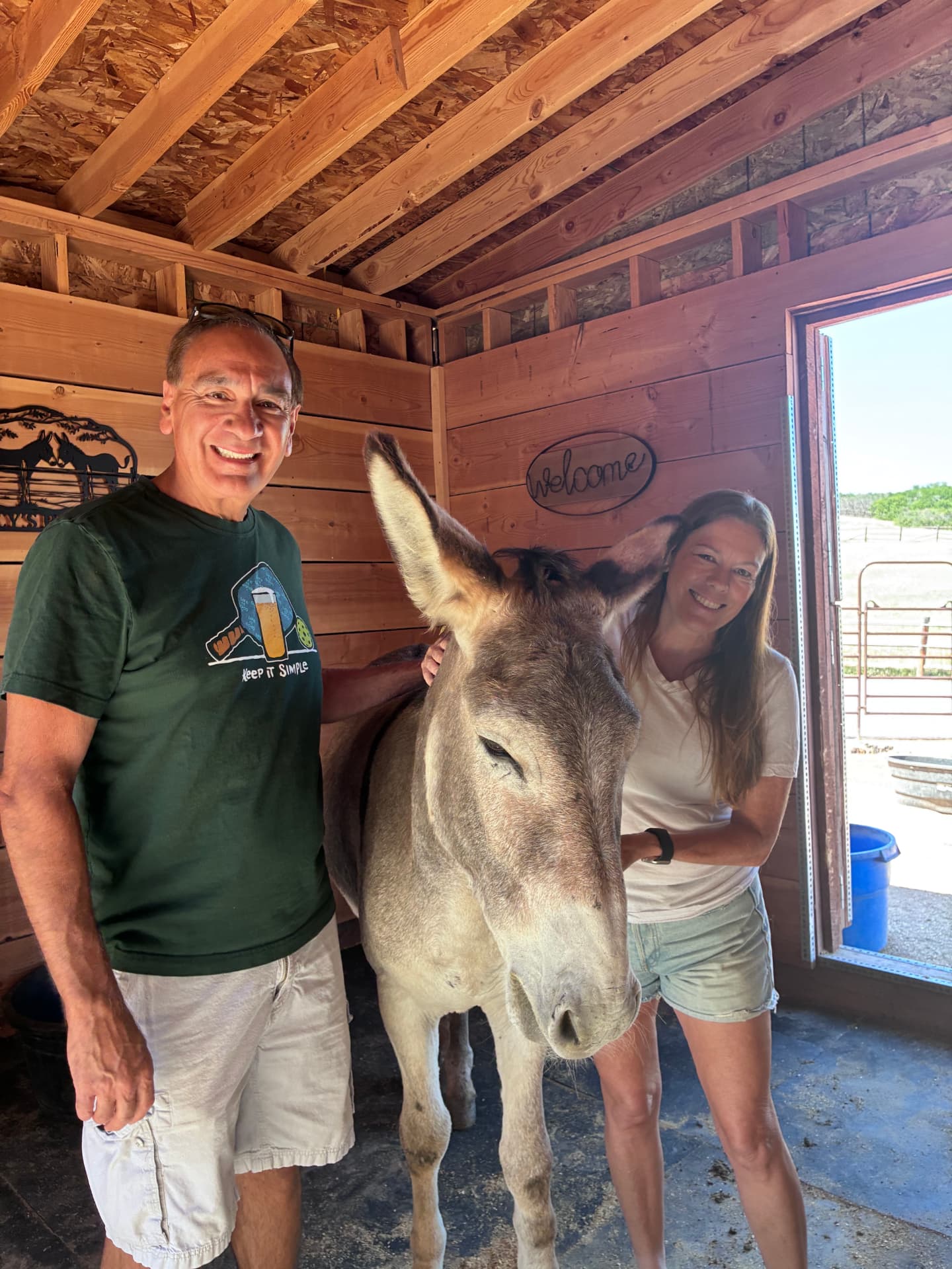 A couple standing on either side of Jackpot in the barn, both smiling